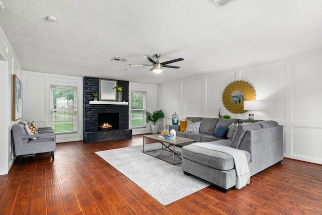 living room featuring a textured ceiling, a brick fireplace, ceiling fan, and dark wood-type flooring