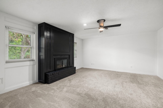 unfurnished living room featuring a textured ceiling, ceiling fan, light carpet, and a brick fireplace