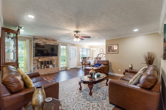 living room with hardwood / wood-style floors, ceiling fan, ornamental molding, a fireplace, and a textured ceiling