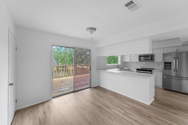 kitchen with kitchen peninsula, stainless steel appliances, decorative backsplash, light wood-type flooring, and sink