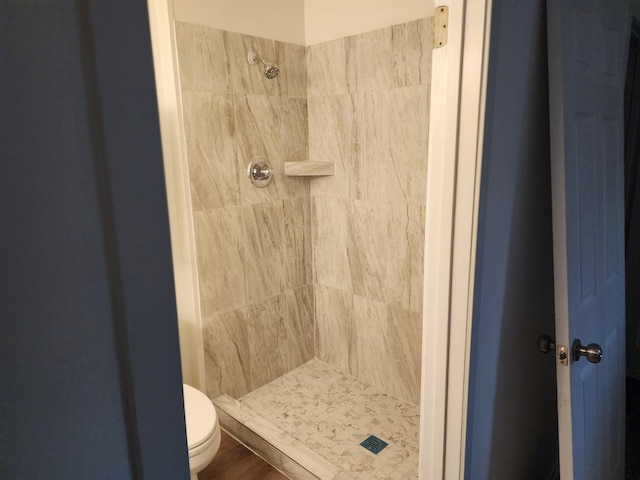 bathroom featuring toilet, wood-type flooring, and a tile shower