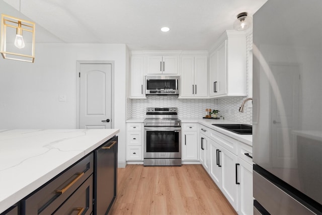 kitchen with light stone countertops, sink, stainless steel appliances, pendant lighting, and white cabinets