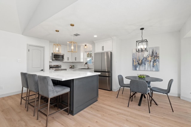 kitchen featuring white cabinetry, a center island, decorative light fixtures, and appliances with stainless steel finishes