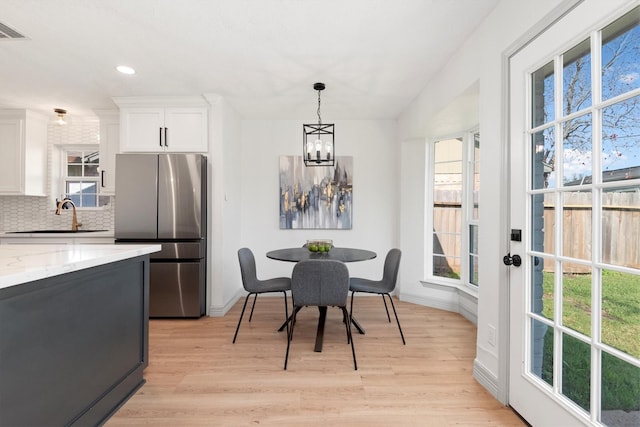 dining room with light wood-type flooring, an inviting chandelier, a wealth of natural light, and sink