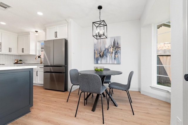 kitchen featuring white cabinets, decorative backsplash, light wood-type flooring, stainless steel refrigerator, and a chandelier