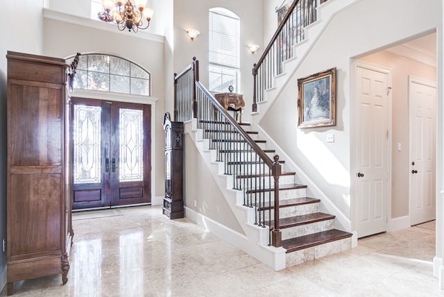 entrance foyer with a high ceiling, french doors, ornamental molding, and a notable chandelier