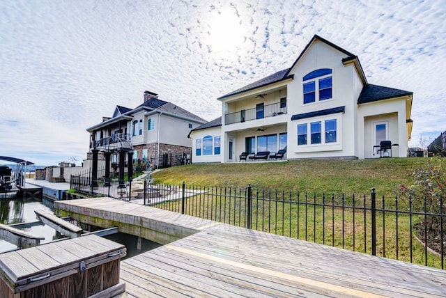 rear view of house with a balcony, a lawn, and a water view