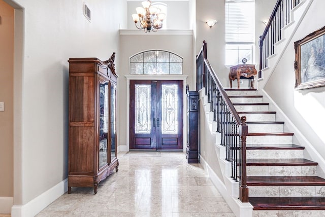 foyer entrance featuring a chandelier, a towering ceiling, and french doors