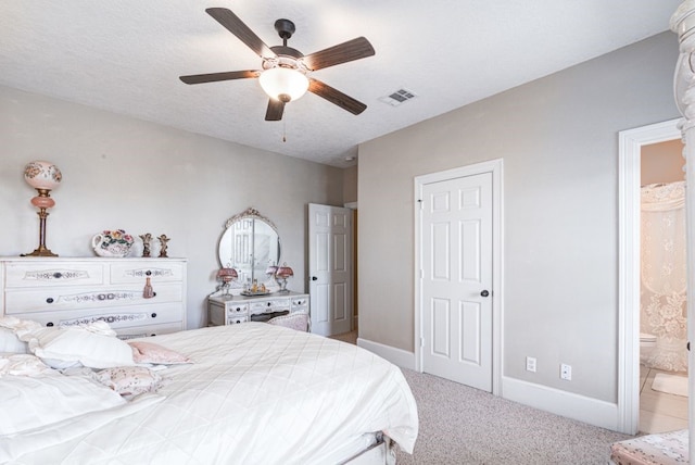 bedroom with a textured ceiling, light colored carpet, connected bathroom, and ceiling fan