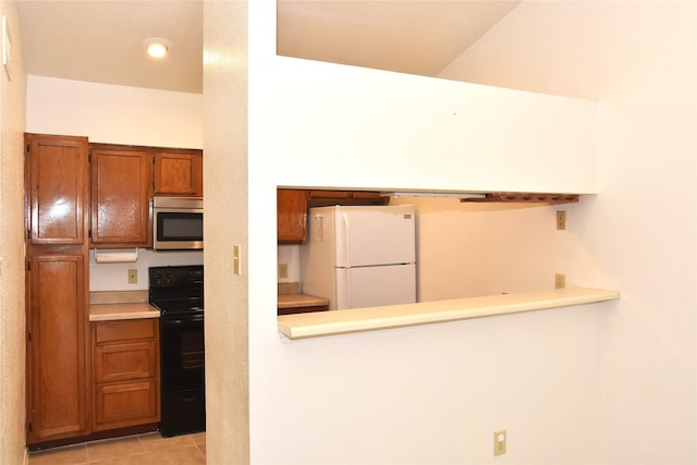 kitchen featuring black range oven, light tile patterned floors, and white refrigerator