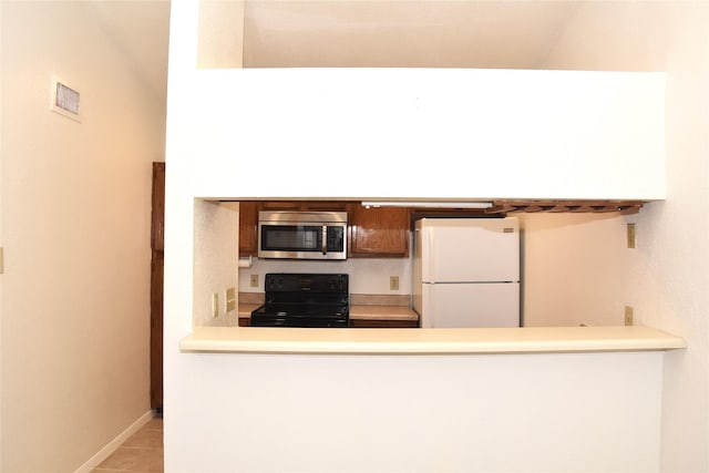 kitchen featuring black range oven, light tile patterned floors, and white refrigerator