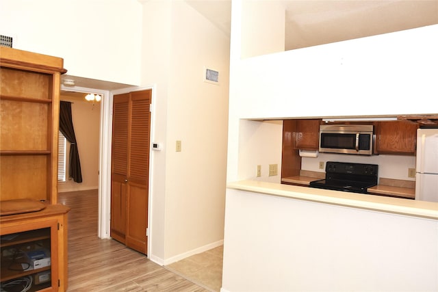 kitchen featuring light hardwood / wood-style floors, a towering ceiling, white refrigerator, and black / electric stove