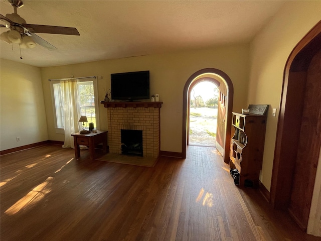 living room with a textured ceiling, ceiling fan, a fireplace, and dark wood-type flooring