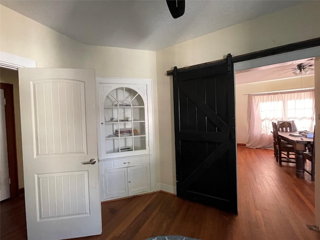 interior space with ceiling fan, a barn door, and dark hardwood / wood-style flooring