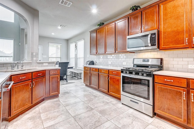 kitchen with appliances with stainless steel finishes, light tile patterned floors, sink, and backsplash