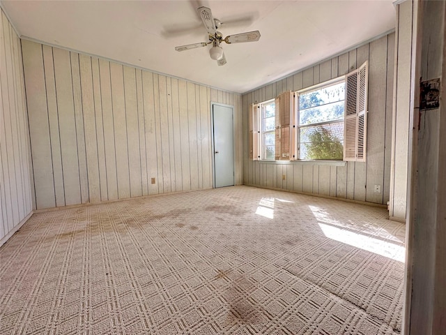 carpeted empty room with ceiling fan and wood walls