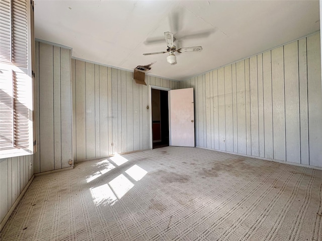 spare room featuring light colored carpet, ceiling fan, and wooden walls