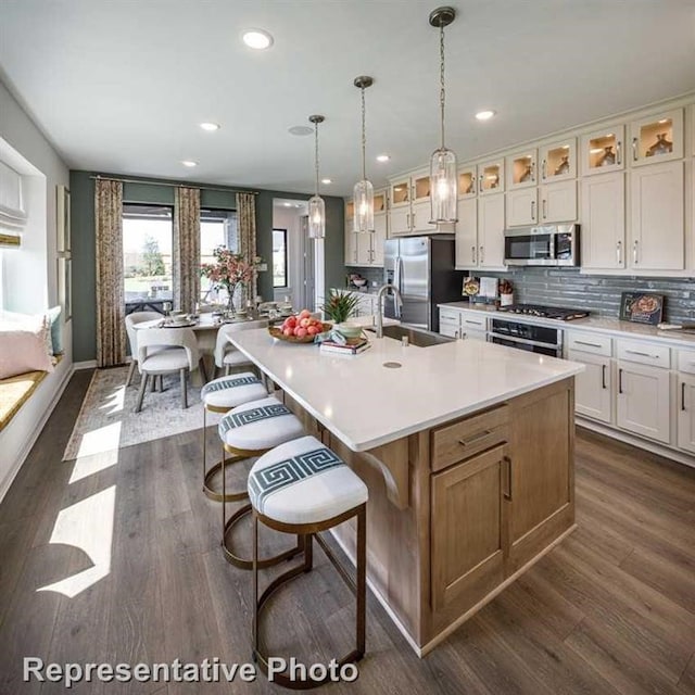 kitchen with stainless steel appliances, sink, a large island with sink, white cabinets, and dark hardwood / wood-style floors