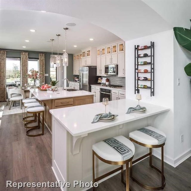 kitchen featuring stainless steel appliances, decorative light fixtures, a breakfast bar, white cabinets, and a center island with sink