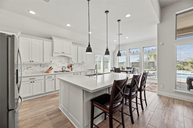 kitchen with a kitchen island with sink, sink, appliances with stainless steel finishes, decorative light fixtures, and white cabinetry