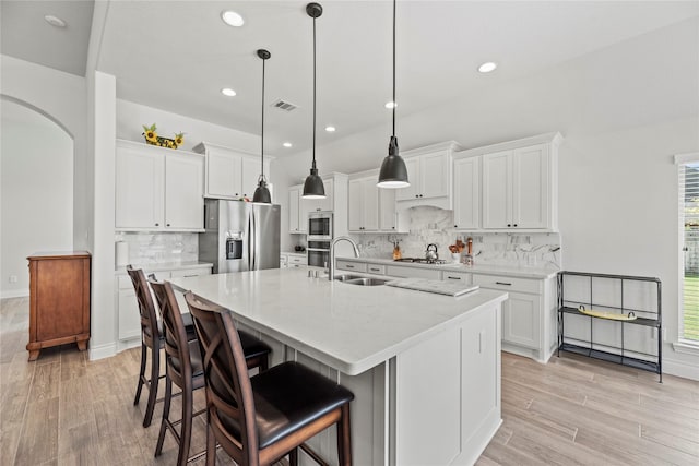 kitchen with white cabinetry, sink, hanging light fixtures, stainless steel appliances, and a kitchen island with sink