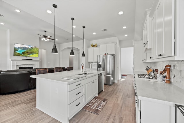 kitchen featuring white cabinetry, sink, hanging light fixtures, stainless steel appliances, and a kitchen island with sink