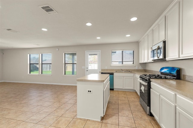 kitchen featuring stainless steel appliances, sink, light tile patterned floors, white cabinets, and a center island