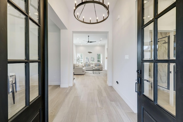 entryway with a high ceiling, french doors, light hardwood / wood-style floors, and ceiling fan with notable chandelier