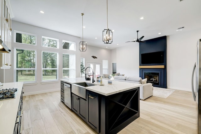 kitchen with light stone countertops, light wood-type flooring, sink, a center island with sink, and a fireplace