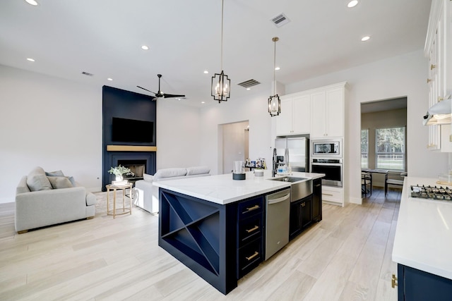 kitchen featuring a kitchen island with sink, hanging light fixtures, white cabinets, and stainless steel appliances