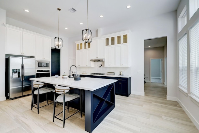 kitchen featuring a kitchen island with sink, hanging light fixtures, appliances with stainless steel finishes, a kitchen bar, and white cabinetry