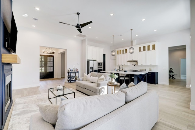 living room with ceiling fan with notable chandelier, light hardwood / wood-style floors, and sink