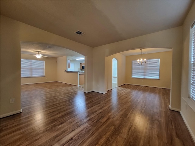 unfurnished living room featuring ceiling fan with notable chandelier, dark wood-type flooring, and a wealth of natural light