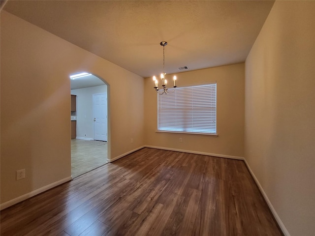 empty room with wood-type flooring and an inviting chandelier