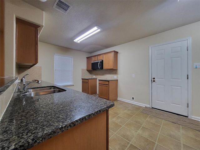 kitchen featuring kitchen peninsula, tasteful backsplash, a textured ceiling, sink, and light tile patterned floors