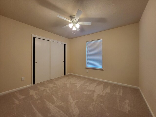 unfurnished bedroom featuring ceiling fan, light colored carpet, a textured ceiling, and a closet