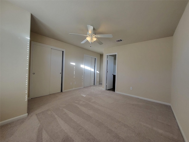 unfurnished bedroom with light carpet, ceiling fan, and multiple closets