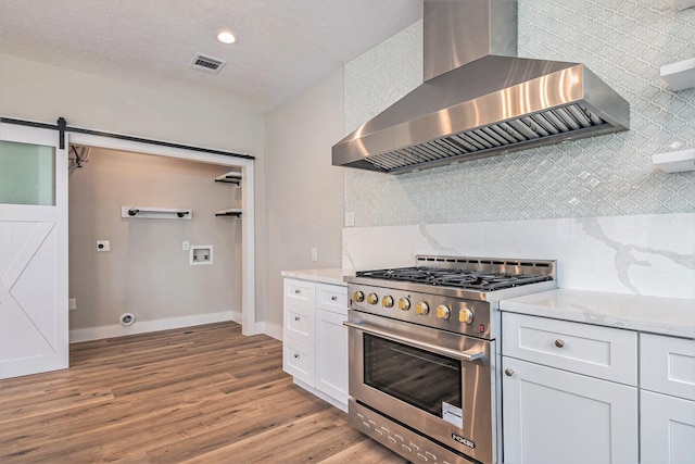 kitchen featuring high end stainless steel range oven, wall chimney exhaust hood, a barn door, light wood-type flooring, and white cabinetry