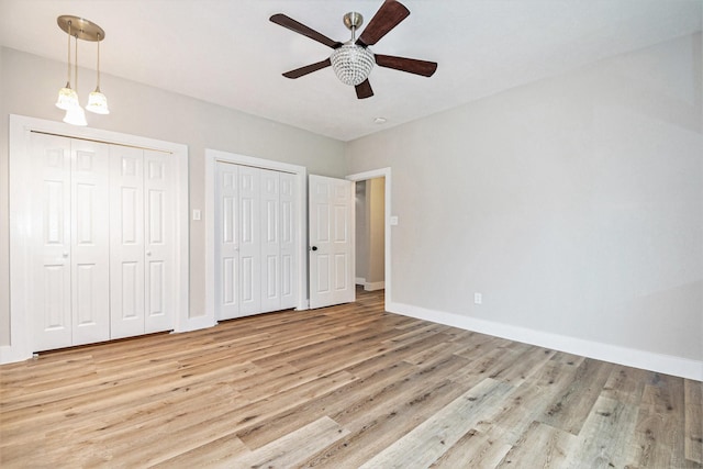 unfurnished bedroom featuring light hardwood / wood-style flooring, ceiling fan, and multiple closets