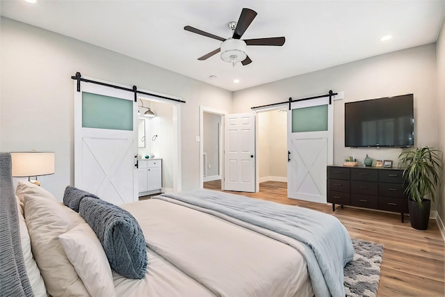 bedroom featuring a barn door, ceiling fan, ensuite bathroom, and light wood-type flooring