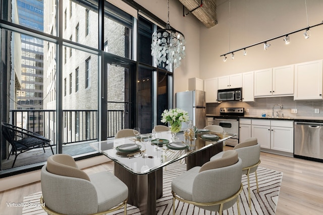 dining area featuring plenty of natural light, sink, light hardwood / wood-style floors, and a high ceiling