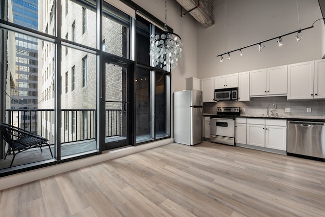 kitchen featuring pendant lighting, a high ceiling, sink, appliances with stainless steel finishes, and light hardwood / wood-style floors