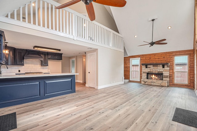 unfurnished living room featuring ceiling fan, a fireplace, high vaulted ceiling, and light wood-type flooring