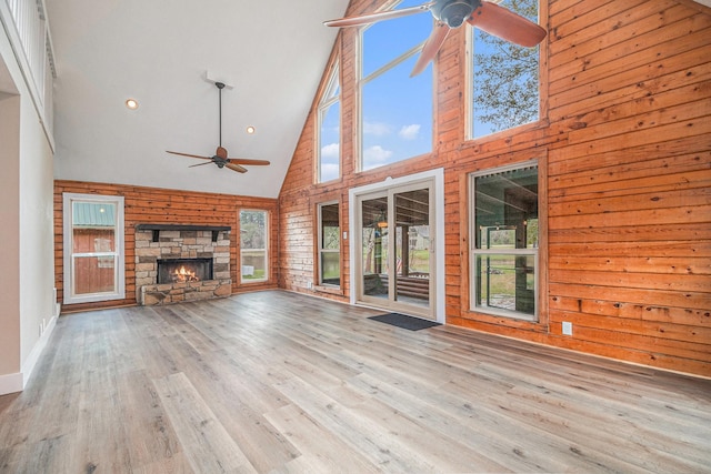 unfurnished living room with a wealth of natural light, wood walls, a fireplace, and high vaulted ceiling