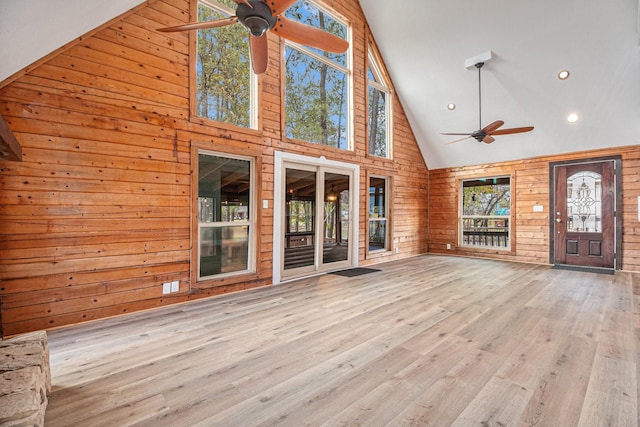 unfurnished living room with light hardwood / wood-style floors, high vaulted ceiling, ceiling fan, and wood walls