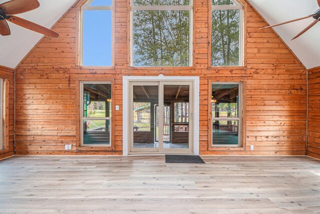 interior space with ceiling fan, light hardwood / wood-style flooring, high vaulted ceiling, and wood walls