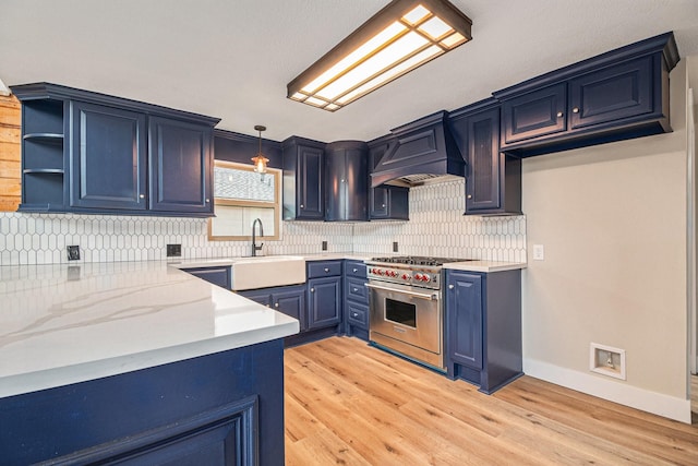 kitchen with blue cabinetry, sink, premium range, decorative light fixtures, and custom range hood