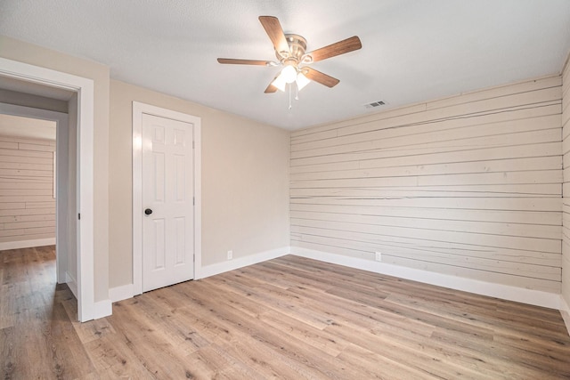 unfurnished room featuring a textured ceiling, light hardwood / wood-style flooring, ceiling fan, and wood walls