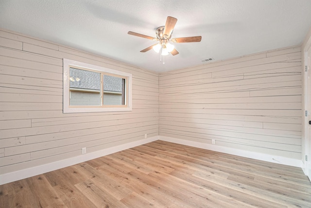 unfurnished room with light wood-type flooring, ceiling fan, and wood walls