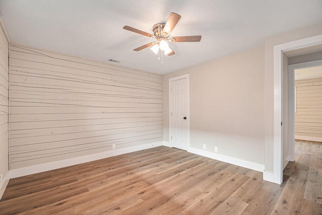 unfurnished room with wooden walls, hardwood / wood-style floors, ceiling fan, and a textured ceiling